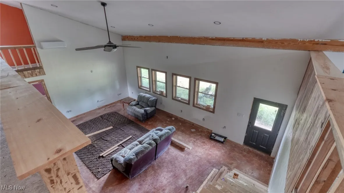 Living area with high vaulted ceiling, ceiling fan, and a wall mounted air conditioner