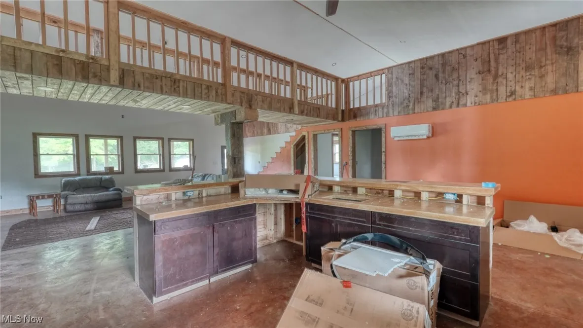 Kitchen with concrete floors, a center island, open floor plan, an AC wall unit, and a towering ceiling