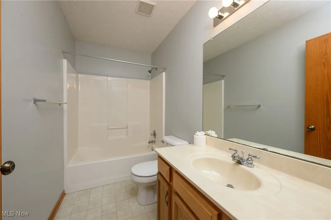 Full bathroom featuring tub / shower combination, vanity, toilet, and a textured ceiling