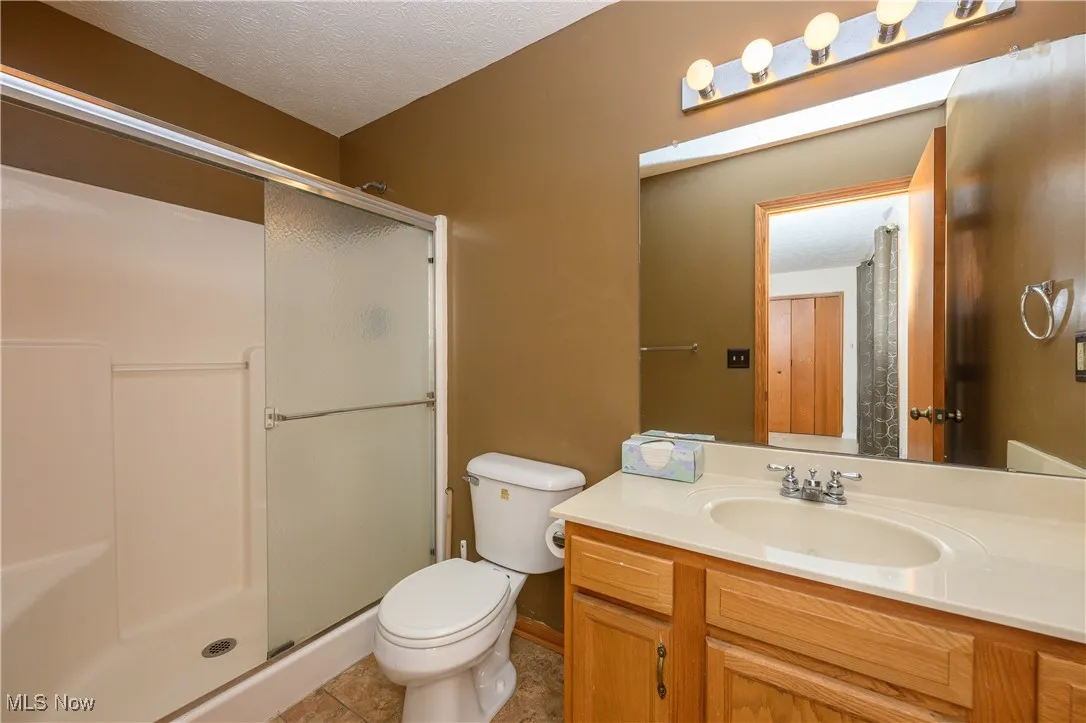 Bathroom with a shower with shower door, vanity, a textured ceiling, toilet, and tile patterned floors