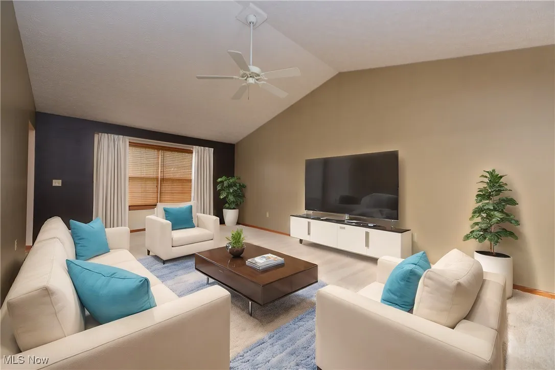 Carpeted living room featuring vaulted ceiling and ceiling fan