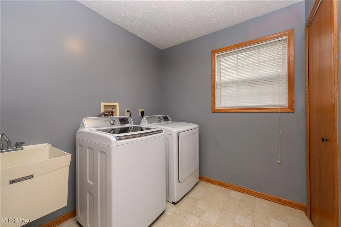 Laundry room featuring sink, independent washer and dryer, and a textured ceiling