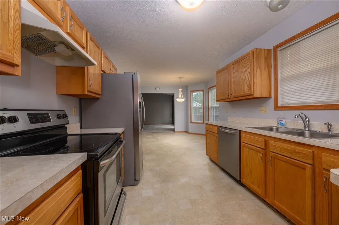 Kitchen featuring a textured ceiling, appliances with stainless steel finishes, decorative light fixtures, and sink