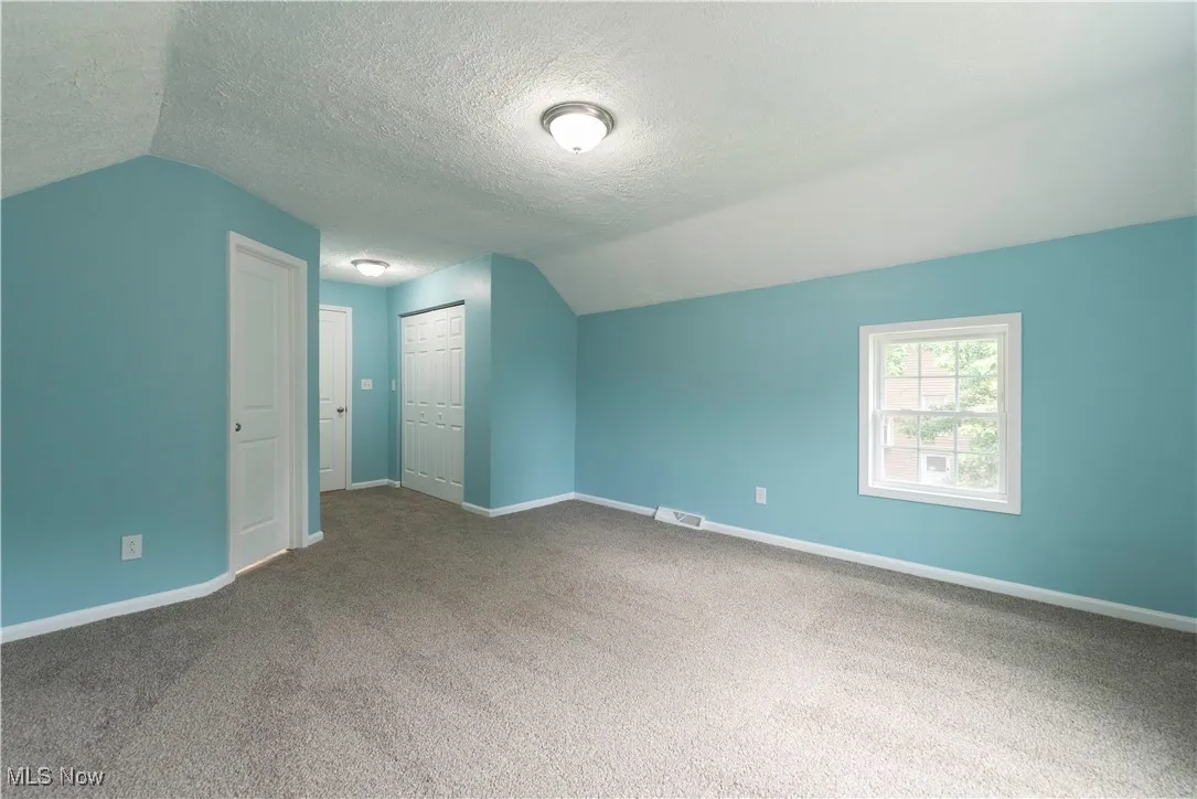 Second floor owner's suite with lofted ceiling, closet, carpet floors, and a textured ceiling