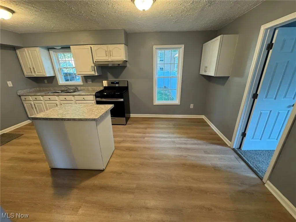 Kitchen with white cabinets, movable island, stainless steel gas range oven, light countertops, light wood-style floors, and a textured ceiling