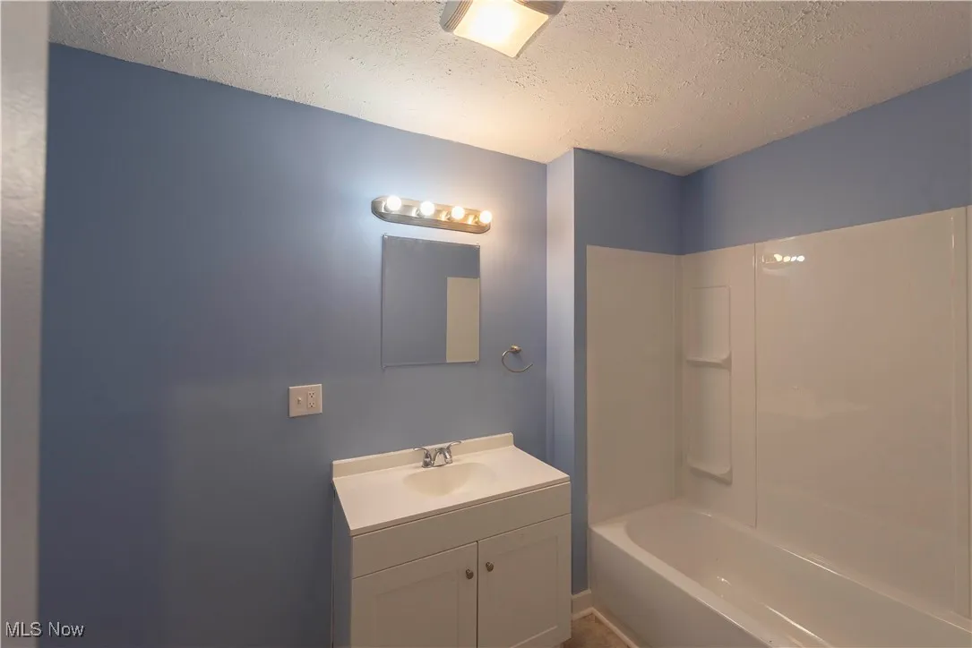 First floor bathroom with a textured ceiling, vanity, and washtub / shower combination