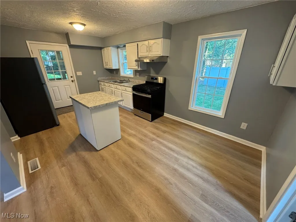 Kitchen with white cabinets, light countertops, movable island, refrigerator, gas range, and a textured ceiling