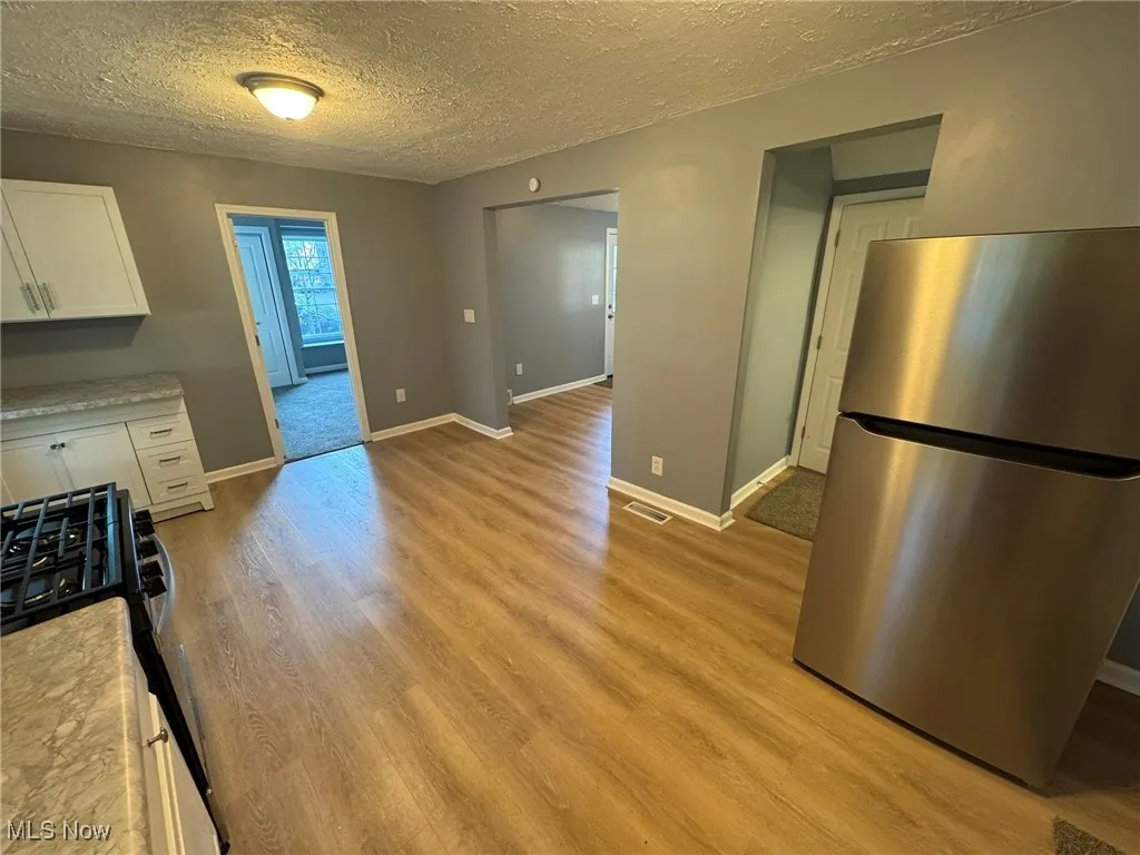 Kitchen with stainless steel refrigerator, black gas range oven, white cabinets, movable island in corner, a textured ceiling, and light wood-style LVT flooring