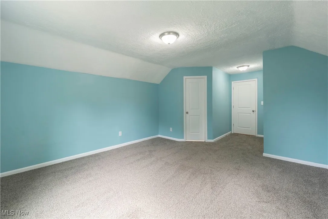 Second floor owner's suite with lofted ceiling, door on left to half bath, carpet flooring, and a textured ceiling