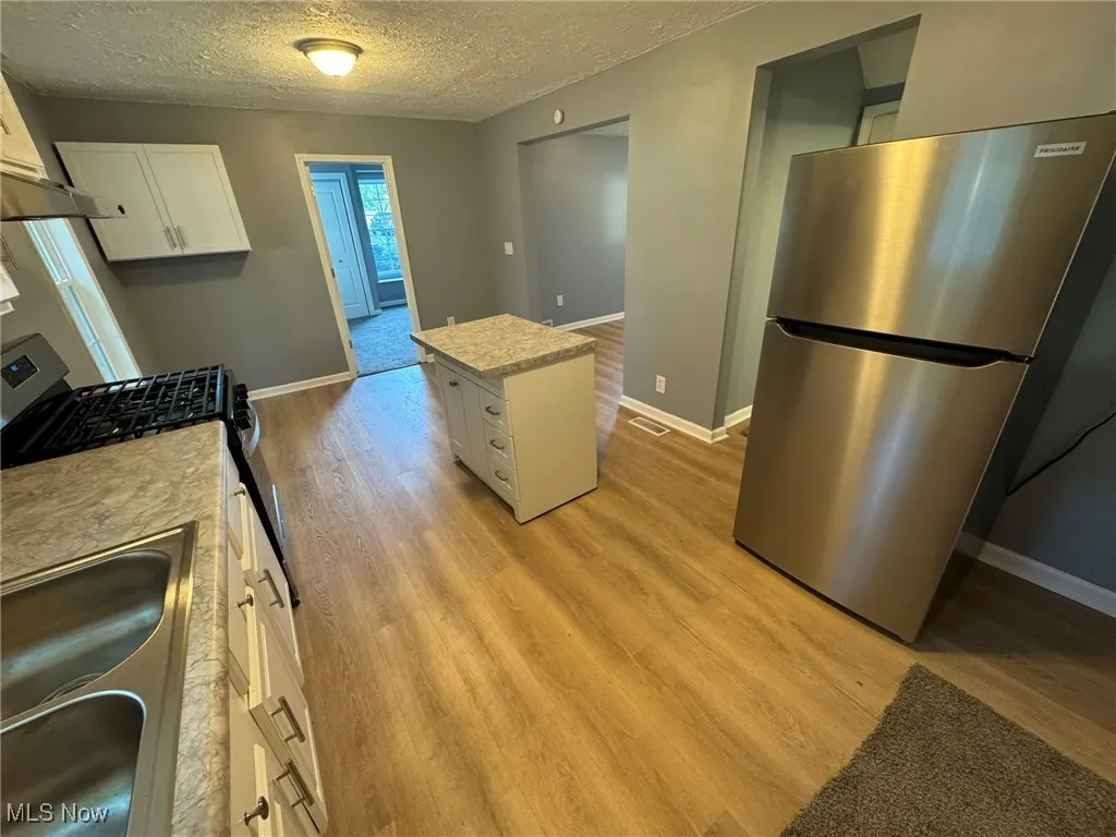 Kitchen with movable island, stainless steel refrigerator, white cabinetry, a textured ceiling, light wood-style LVT floors, and a center island