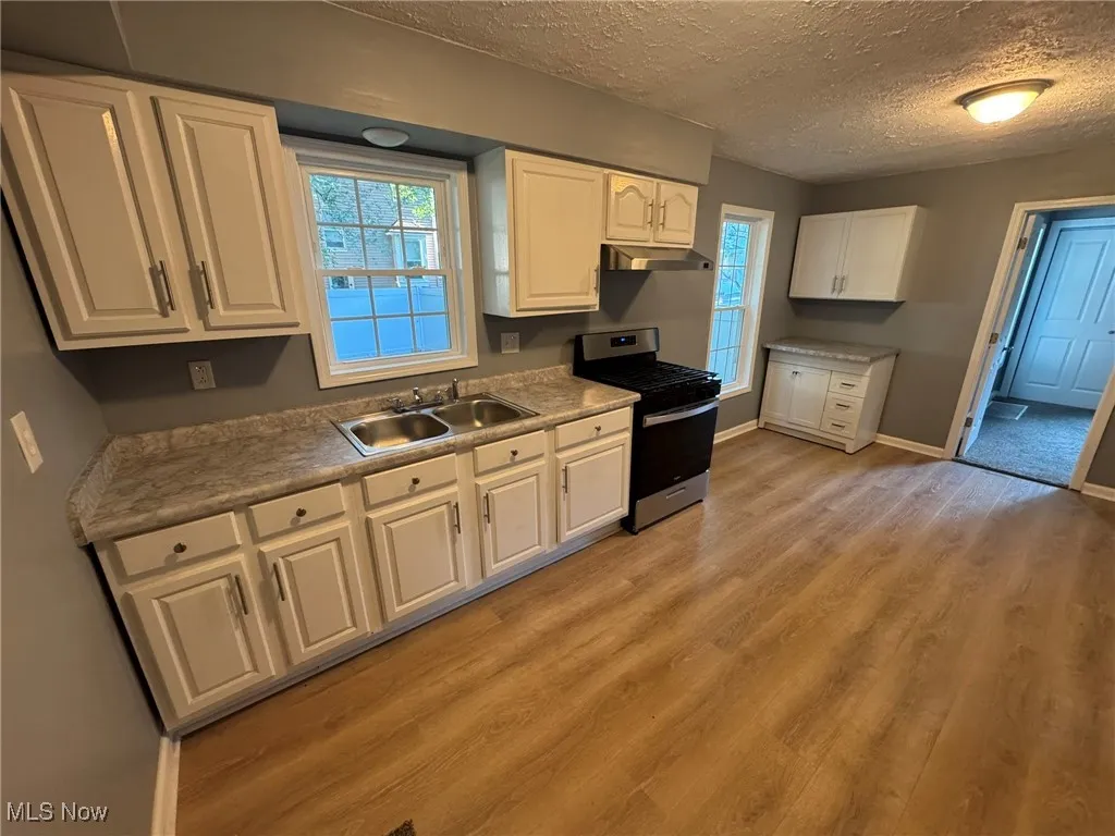 Kitchen with movable island in corner, stainless steel range with gas cooktop, white cabinetry, light countertops, light wood finished floors, and a textured ceiling
