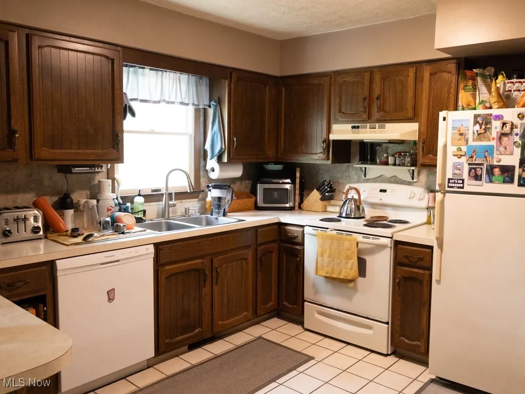 Kitchen with white appliances, light countertops, backsplash, under cabinet range hood, and a textured ceiling
