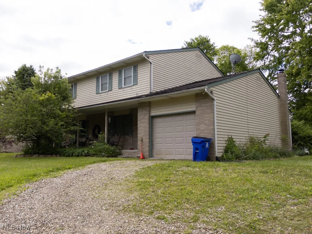 View of front of house featuring driveway, brick siding, a garage, a chimney, and a front lawn