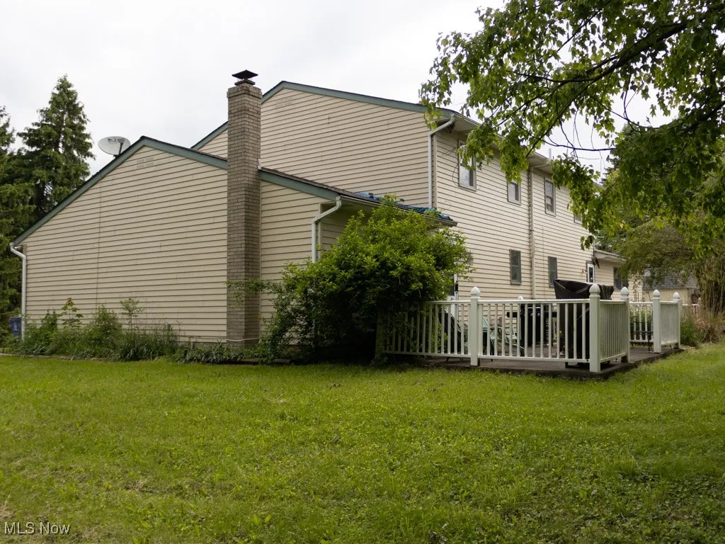 View of property exterior with a yard, a chimney, and a deck