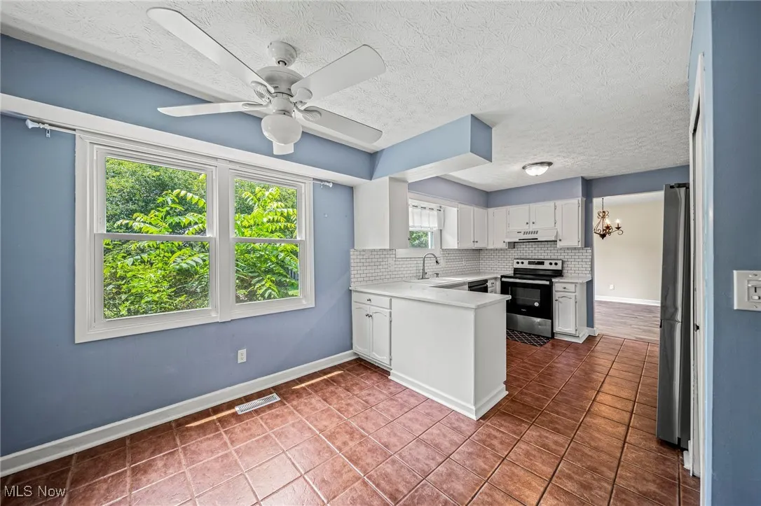 Kitchen with electric stove, under cabinet range hood, a peninsula, tasteful backsplash, and light countertops