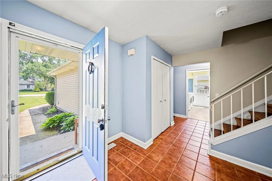 Entryway with independent washer and dryer, tile patterned flooring, stairway, and a textured ceiling