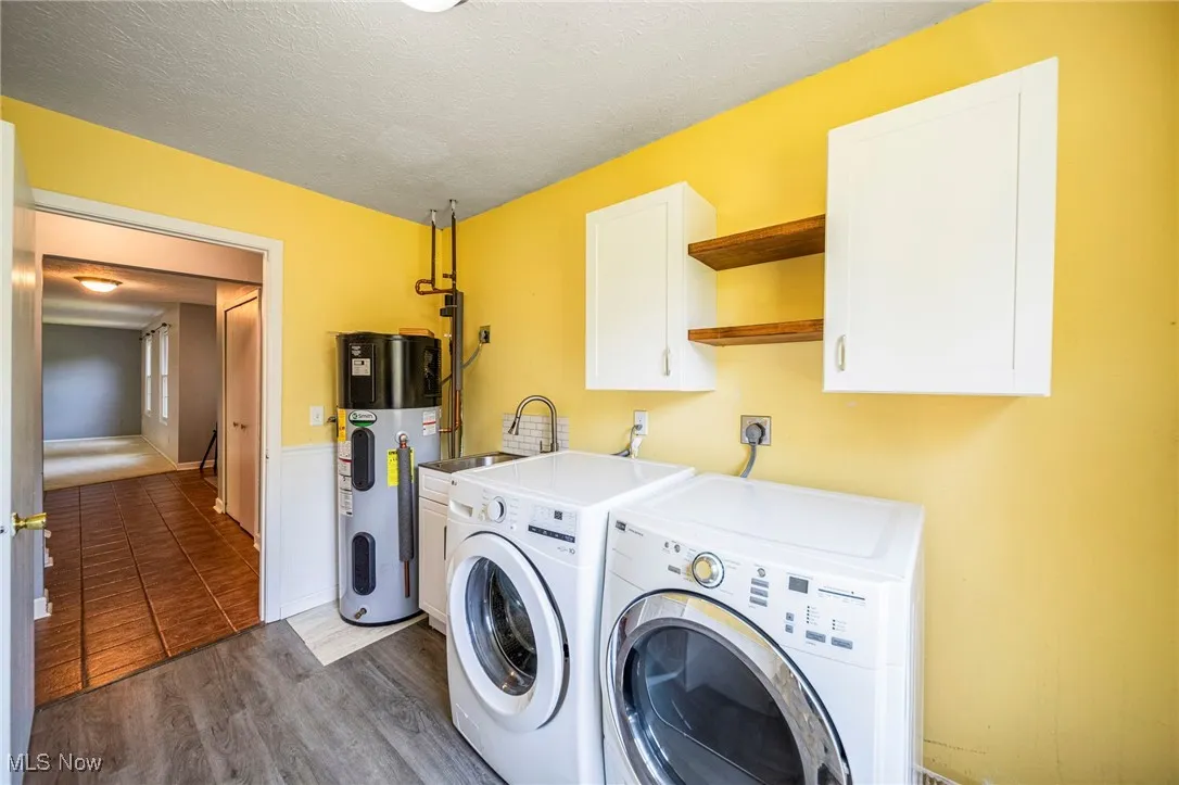 Laundry area featuring heat pump water heater, cabinet space, washer and clothes dryer, wood finished floors, and a textured ceiling