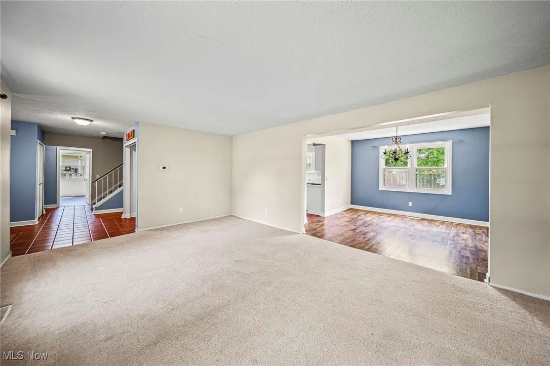 Empty room featuring carpet, stairs, and a chandelier