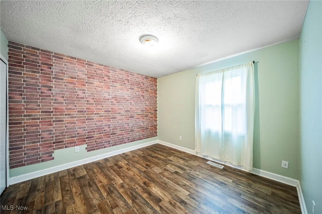 Spare room with wood finished floors, brick wall, and a textured ceiling