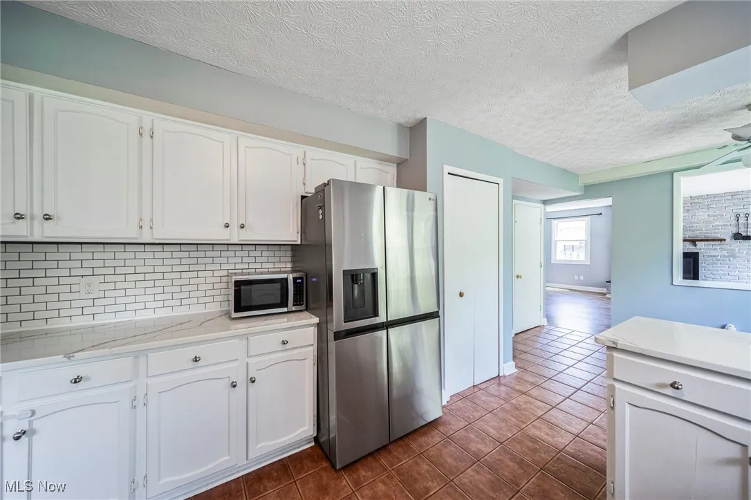 Kitchen featuring stainless steel appliances, decorative backsplash, white cabinetry, a textured ceiling, and dark tile patterned floors