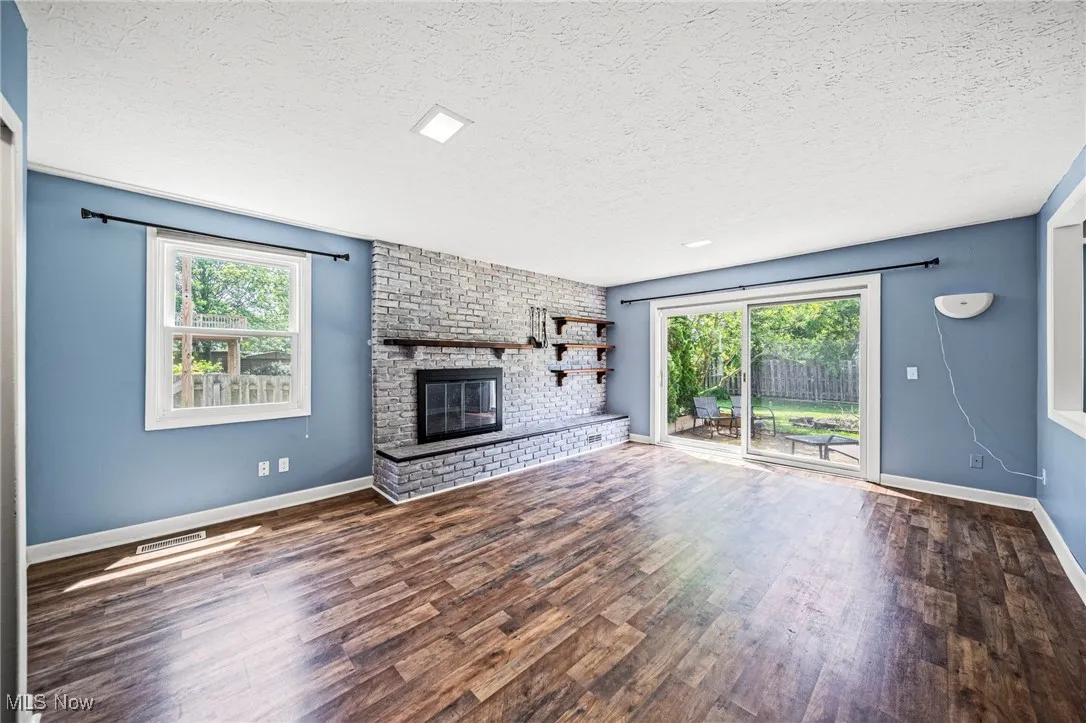 Unfurnished living room with a textured ceiling, healthy amount of natural light, wood finished floors, and a brick fireplace