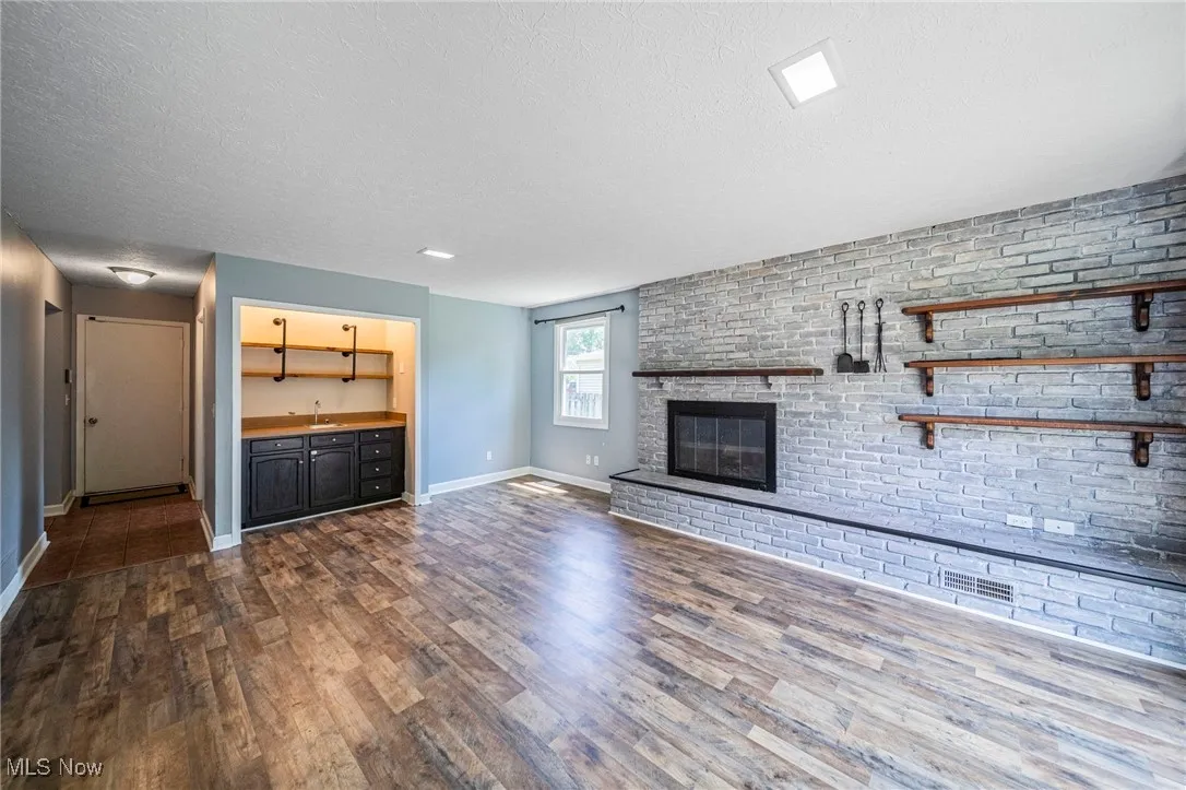 Unfurnished living room featuring dark wood-style flooring, a textured ceiling, a fireplace, and wet bar
