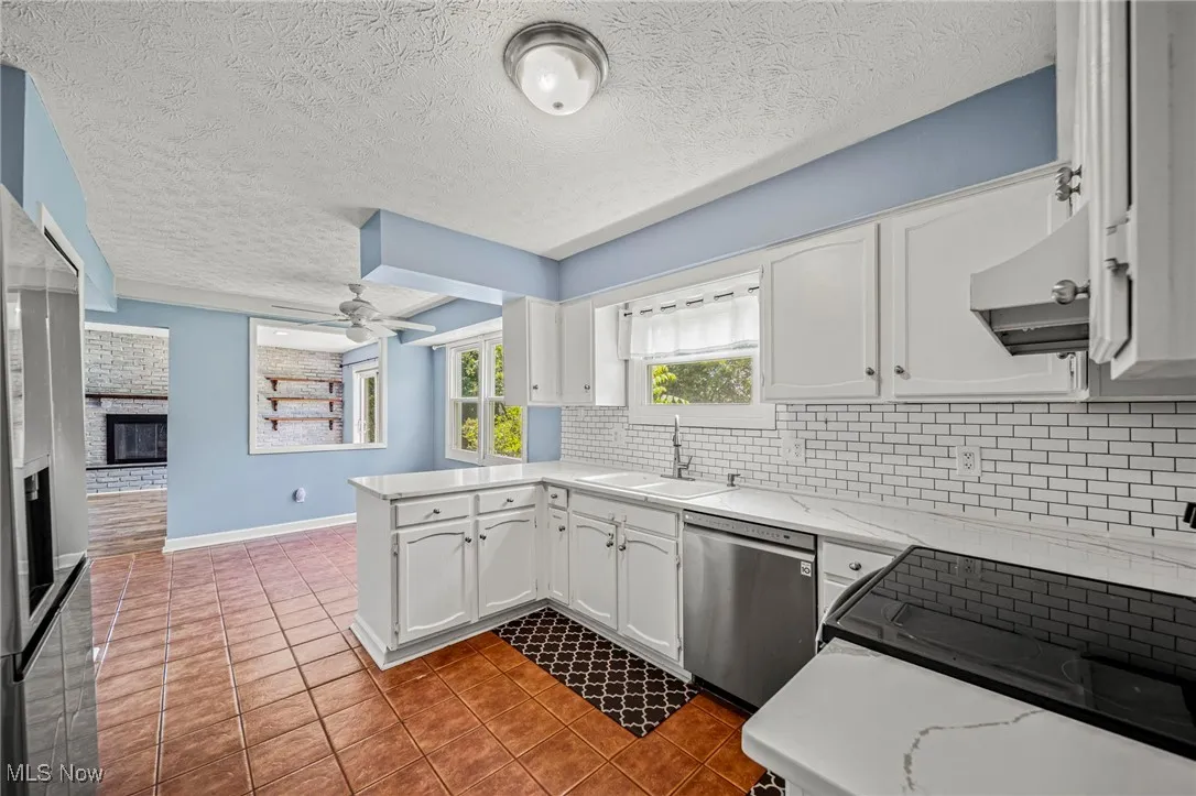 Kitchen with dishwasher, wall chimney exhaust hood, tile patterned floors, decorative backsplash, and white cabinetry