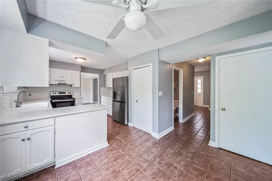 Kitchen featuring electric range, stainless steel fridge, under cabinet range hood, backsplash, and a peninsula