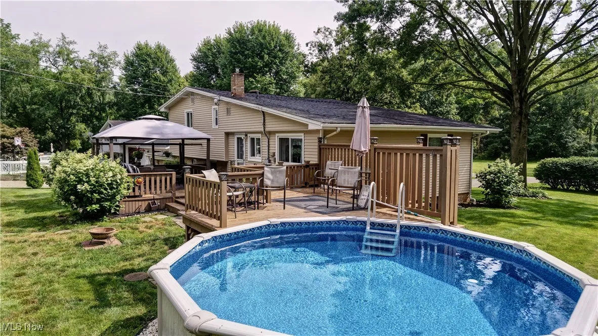 Outdoor pool with a gazebo, a deck, a lawn, view of wooded area, and outdoor dining space