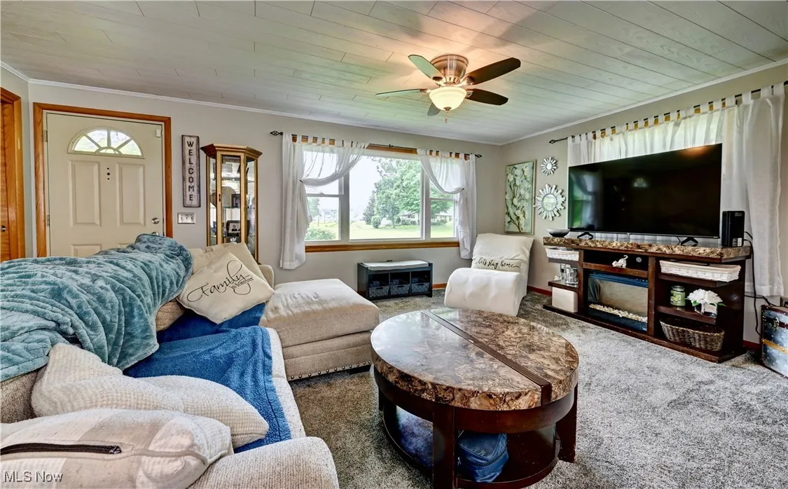 Living room with carpet flooring, ornamental molding, wooden ceiling, and a ceiling fan