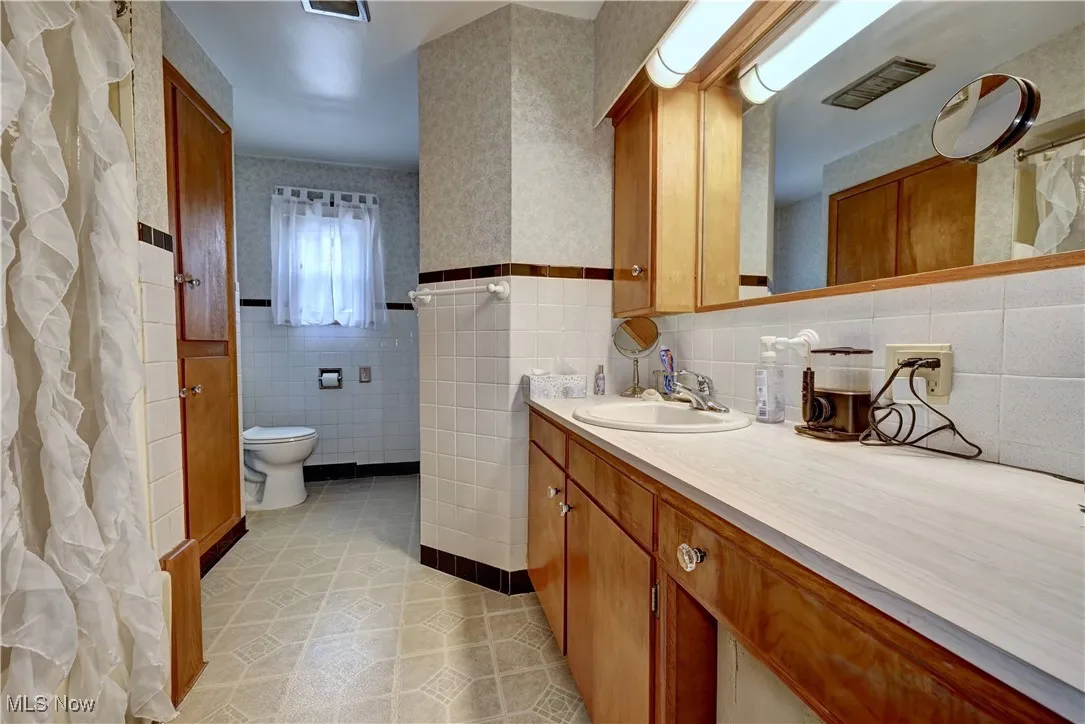 Bathroom with tile walls, vanity, and wallpapered walls