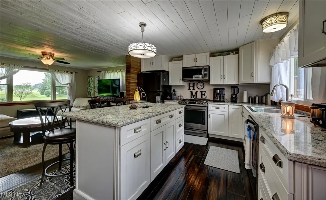Kitchen with black appliances, dark wood-type flooring, a kitchen island, light stone countertops, and wood ceiling