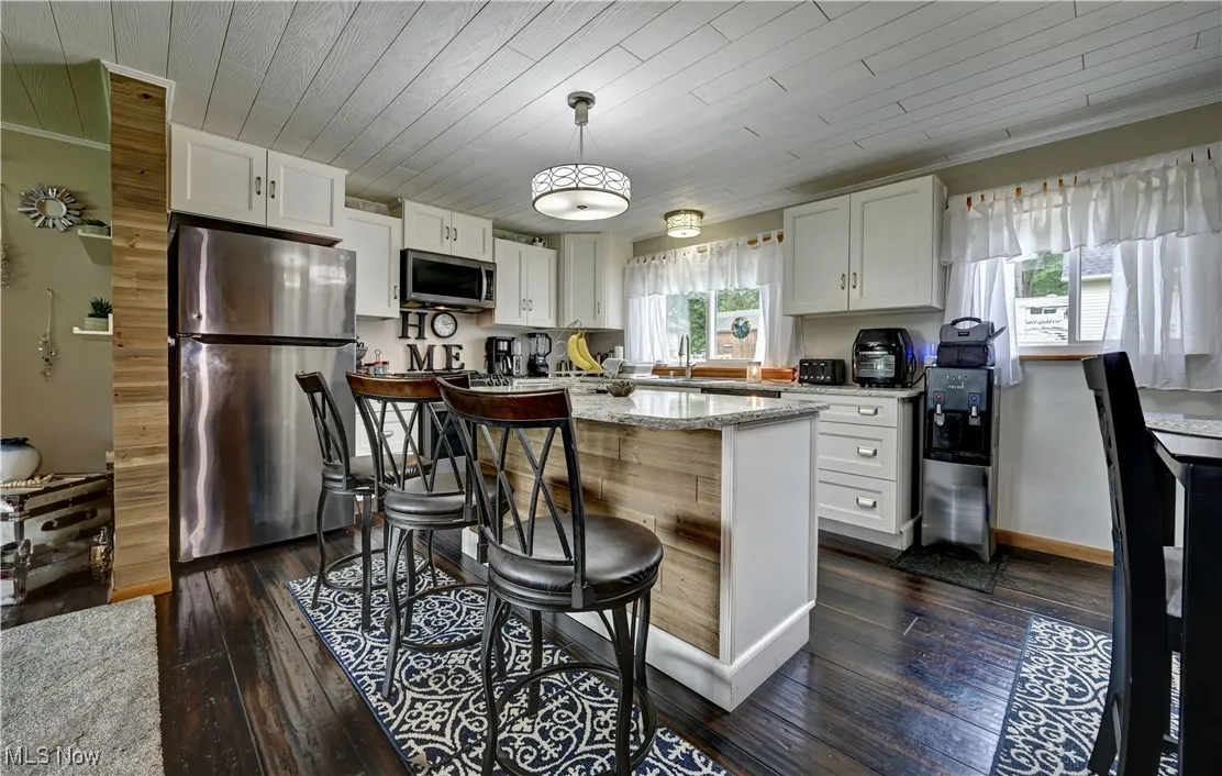 Kitchen with appliances with stainless steel finishes, dark wood finished floors, white cabinets, light stone counters, and wood ceiling