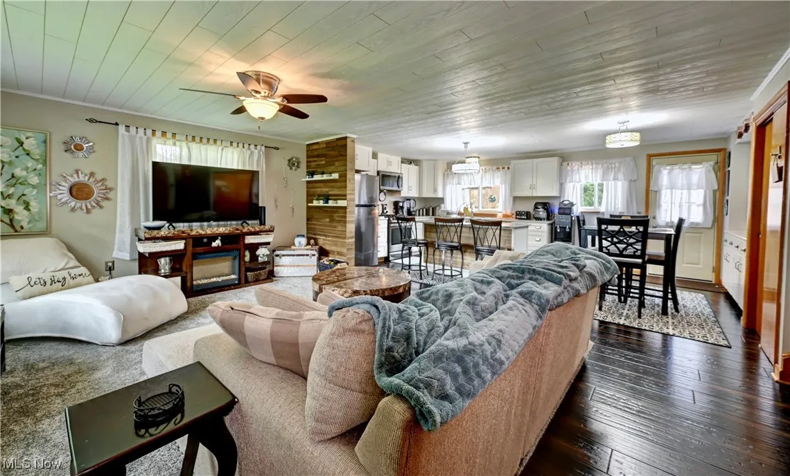Living area featuring a ceiling fan, dark wood-type flooring, ornamental molding, and wooden ceiling
