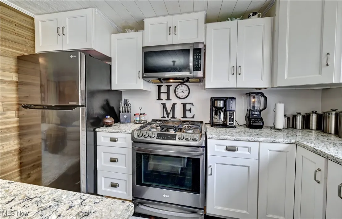 Kitchen with appliances with stainless steel finishes, white cabinets, wooden ceiling, and light stone countertops