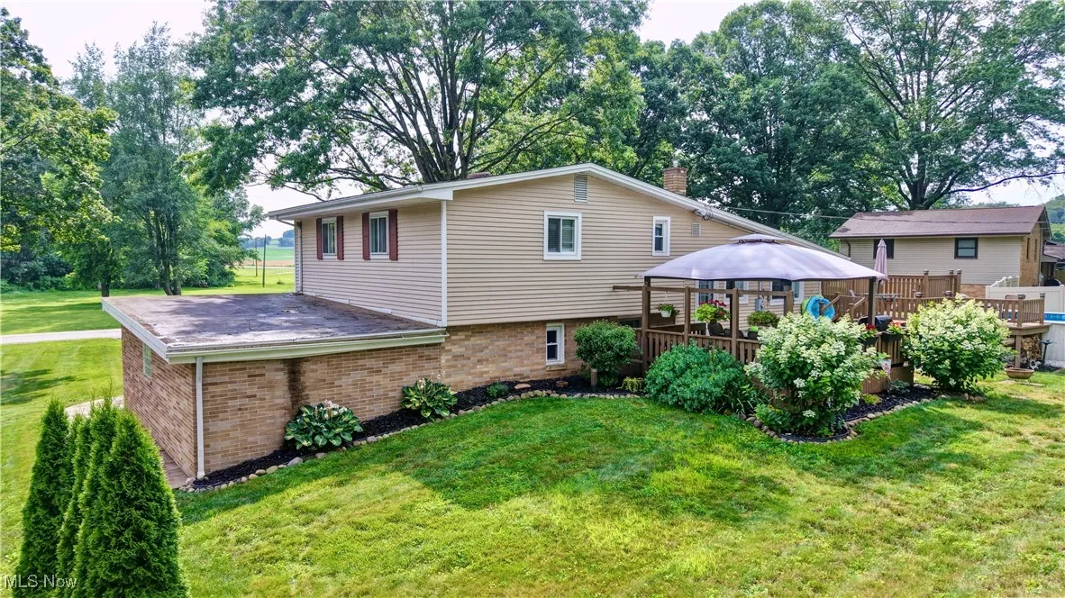 Back of house with a gazebo, brick siding, a lawn, a wooden deck, and a chimney
