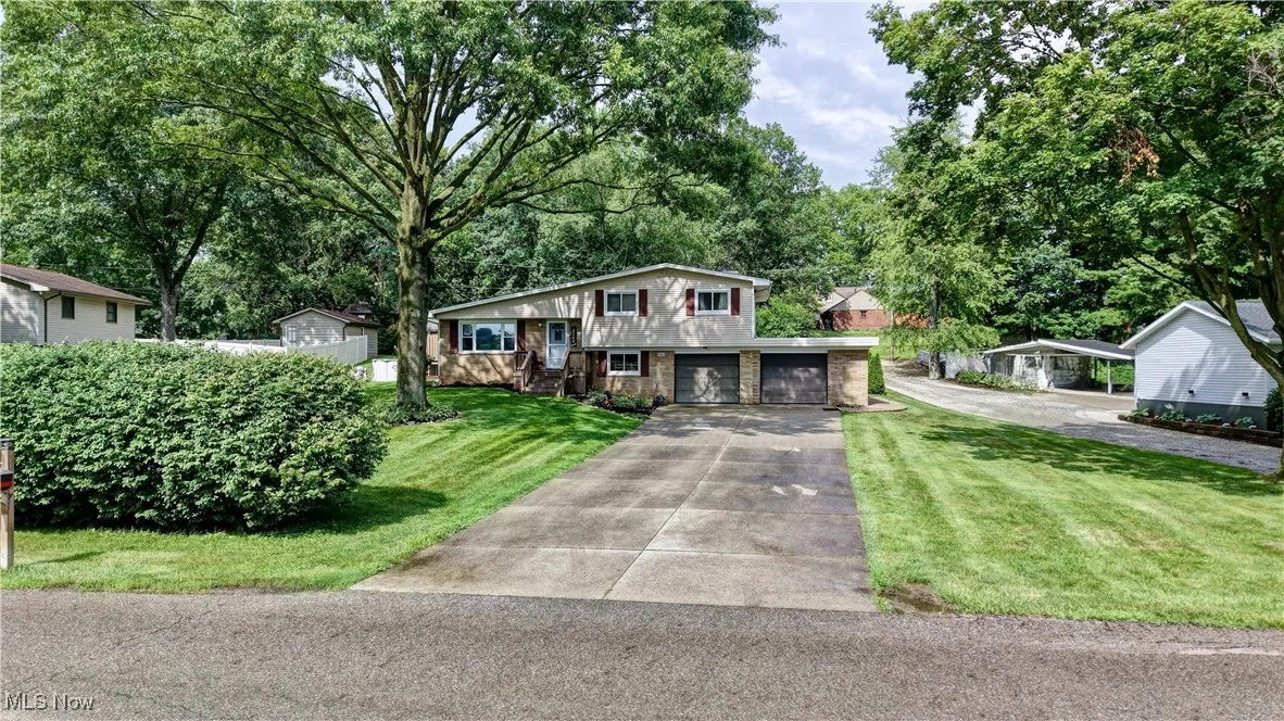 Split level home featuring concrete driveway, stone siding, a front yard, and an attached garage