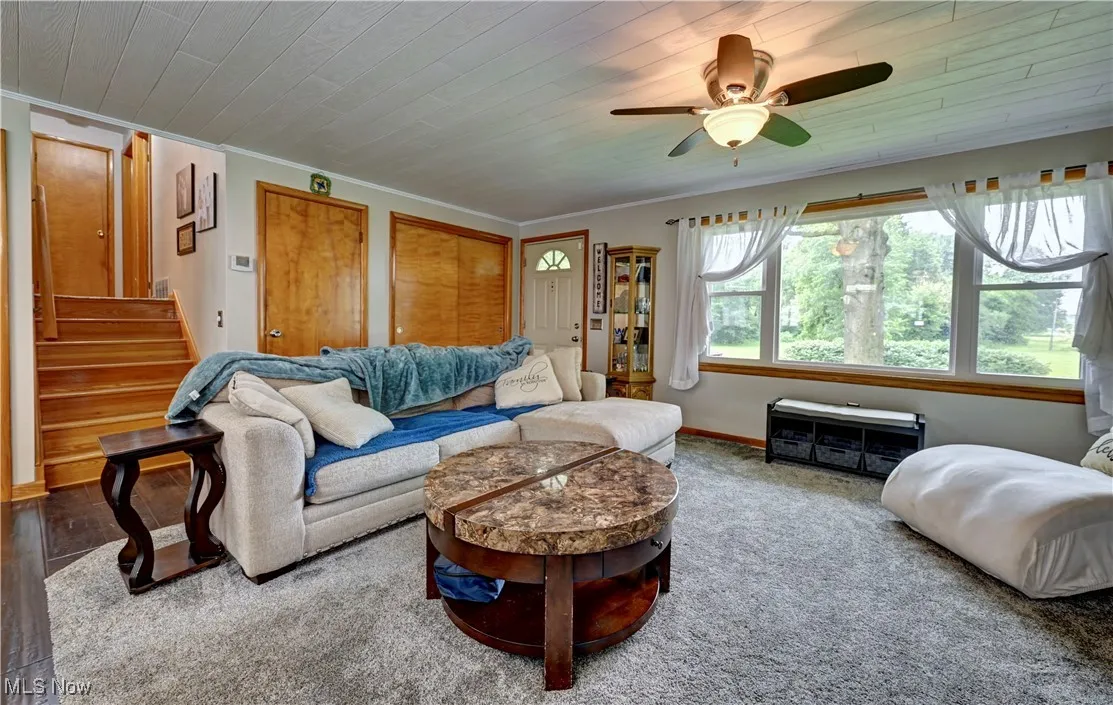 Living area featuring a ceiling fan, crown molding, stairway, wooden ceiling, and carpet