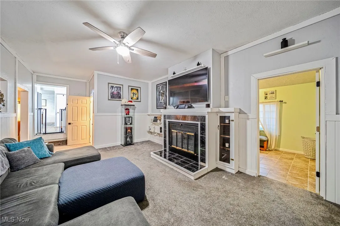 Carpeted living room featuring a ceiling fan, a tiled fireplace, and a textured ceiling