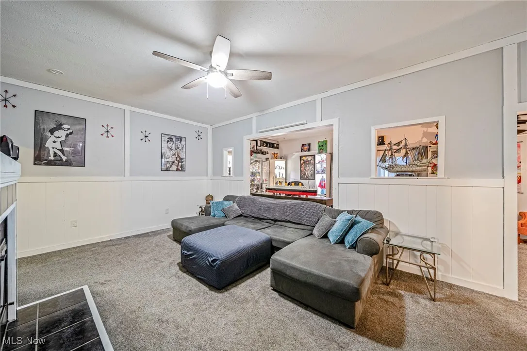 Carpeted living area with ceiling fan, a decorative wall, crown molding, and a wainscoted wall