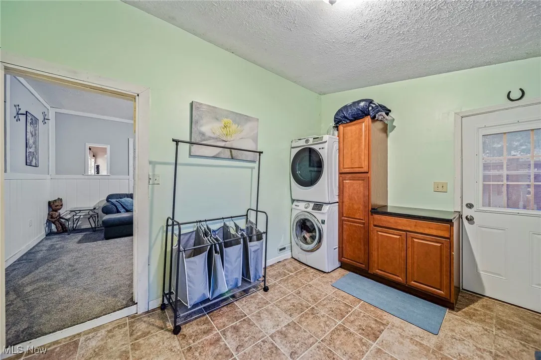 Laundry area featuring cabinet space, stacked washer / drying machine, and a textured ceiling