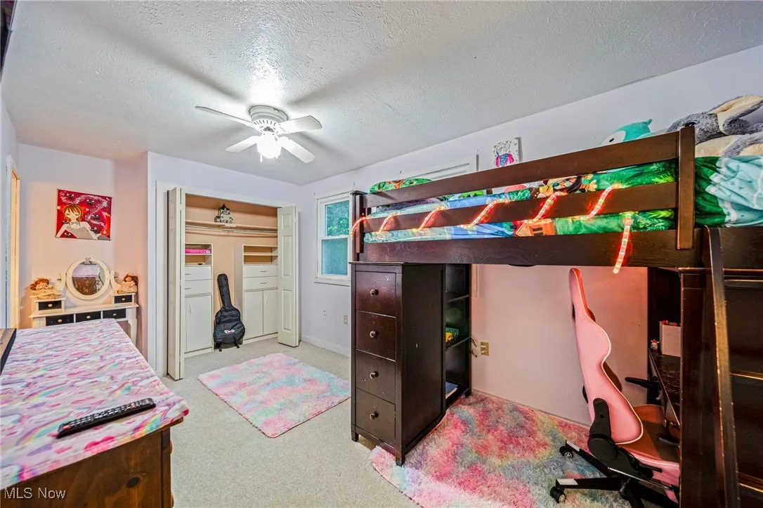 Carpeted bedroom with a textured ceiling, ceiling fan, and a closet