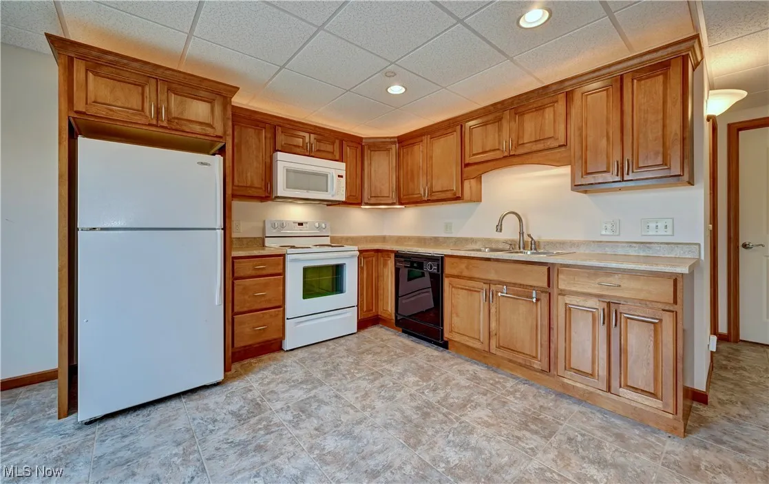 Kitchen featuring white appliances, light countertops, brown cabinets, a paneled ceiling, and recessed lighting