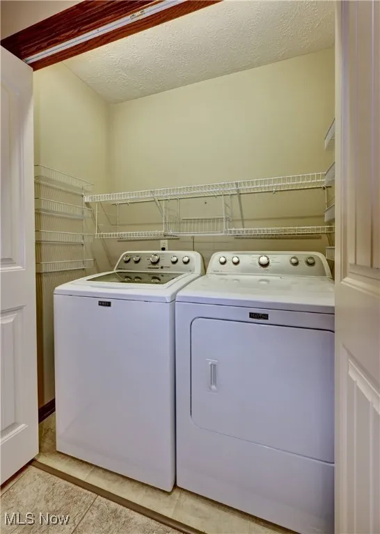 Washroom with washing machine and dryer, a textured ceiling, and light tile patterned flooring