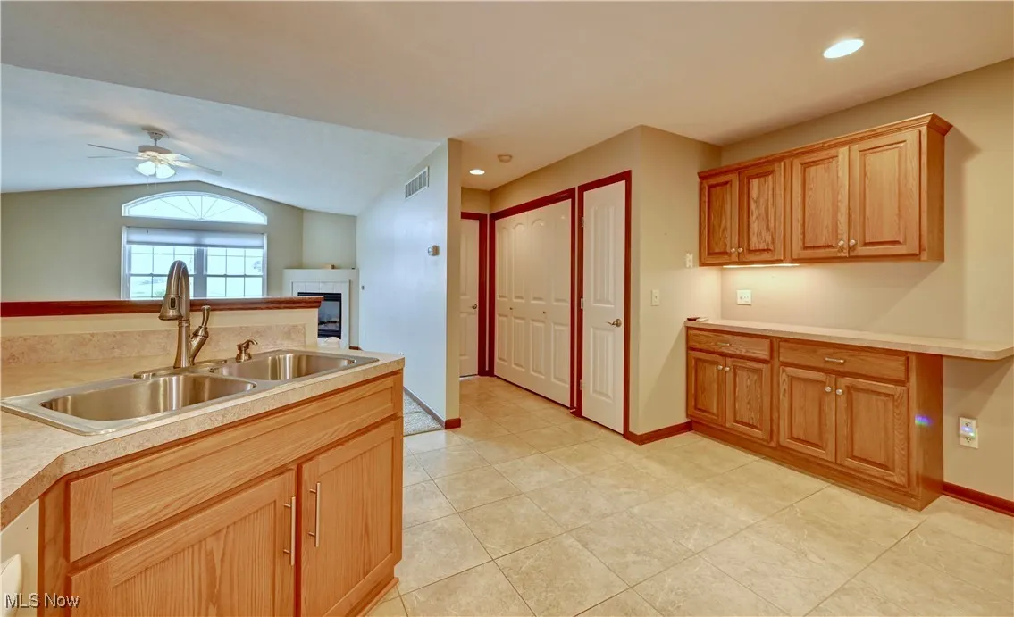 Kitchen featuring vaulted ceiling, a fireplace, light tile patterned flooring, light countertops, and a ceiling fan