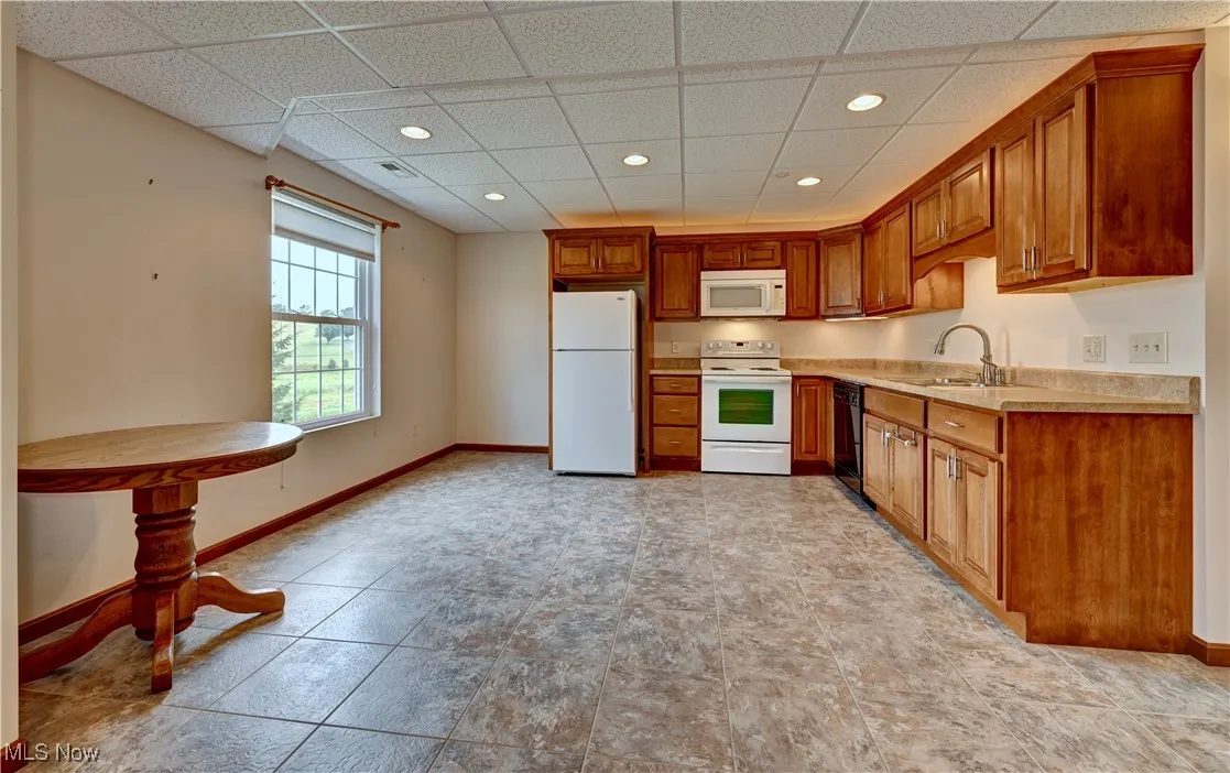 Kitchen featuring white appliances, light countertops, brown cabinetry, a drop ceiling, and recessed lighting