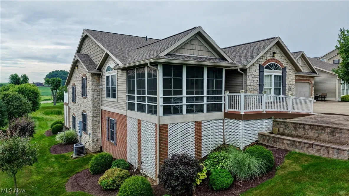 View of property exterior with stone siding, a sunroom, a garage, driveway, and roof with shingles