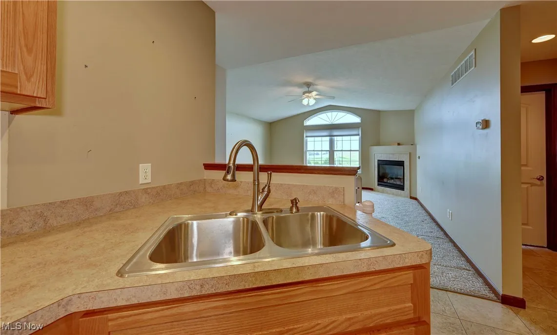 Kitchen with vaulted ceiling, ceiling fan, light tile patterned floors, a tiled fireplace, and light countertops