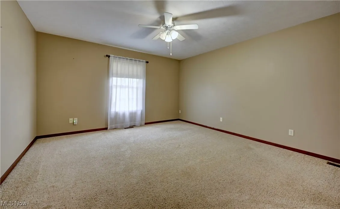 Carpeted spare room with ceiling fan and baseboards