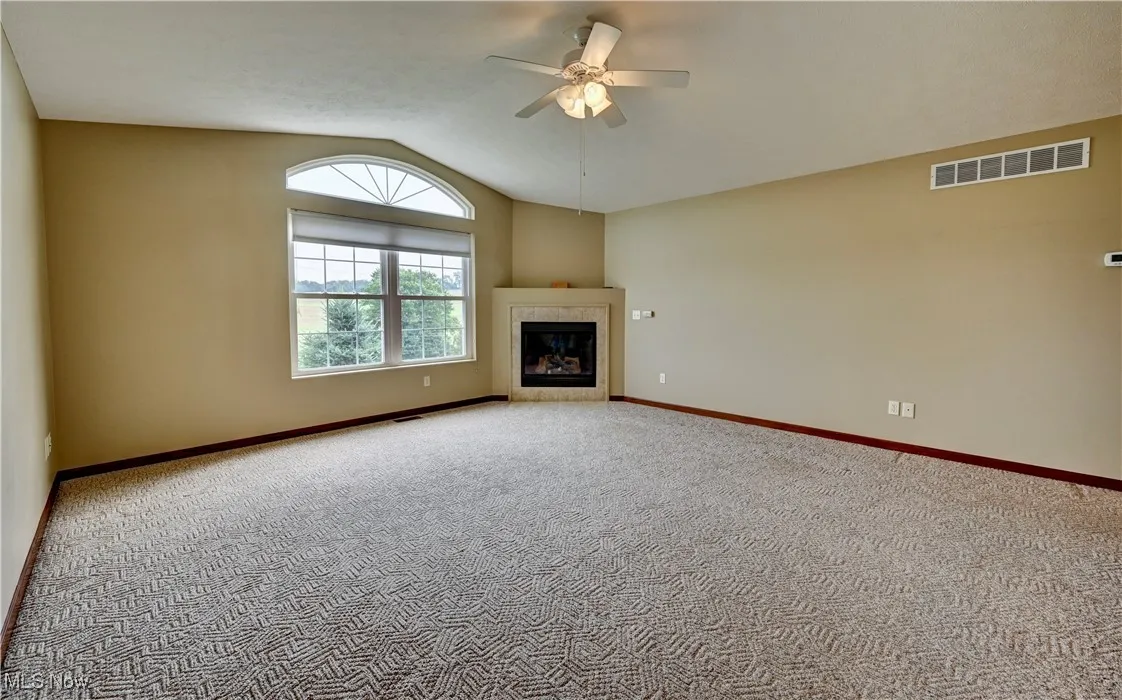 Unfurnished living room featuring vaulted ceiling, ceiling fan, carpet, and a fireplace